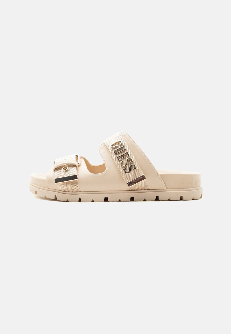 Sandale beige à enfiler avec semelle épaisse, deux sangles réglables et logo métallique "GUESS" sur la bride supérieure.