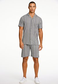 Camicetta a maniche corte a righe e pantaloni corti coordinati in tessuto blu e grigio. Presenta un design con bottoni e una vestibilità morbida con una texture liscia.