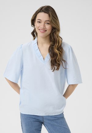 Blouse bleu clair à manches courtes avec un col en V volanté, réalisée en tissu lisse, avec une coupe décontractée et une texture subtile.