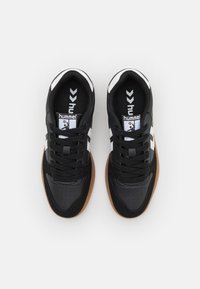 Black athletic shoes with a textured leather and suede upper, white stripes, and a rubber gum sole. Laced design with perforated toe box.