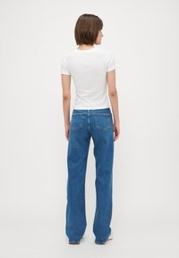 T-shirt blanc à manches courtes avec un col rond, associé à un jean droit bleu taille haute avec poches arrière et une finition soignée.