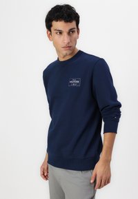 Sudadera azul marino en mezcla de algodón, con cuello redondo, puños y dobladillo acanalados, presenta un parche de logo bordado en el pecho.