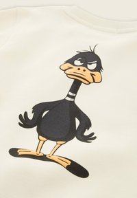 Felpa crema con una stampa di un'anatra cartoon nera e arancione con un'espressione caricaturale, posizionata su uno sfondo di tessuto.