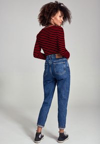Camicia a maniche lunghe a righe rosse e nere, jeans in denim blu a vita alta, con risvolti e tasche posteriori, abbinati a sneaker nere.