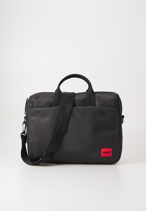 Čierna taška na laptop vyrobená z hladkého nylonu, s dvojitými uchami, odnímateľným ramenným popruhom a červenou nášivkou loga na prednej strane.