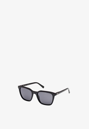 Zwarte rechthoekige zonnebril met donkere lenzen. Dikke kunststof montuur met een glanzende afwerking. Aan de zijkant bevindt zich een klein metalen accent bij de scharnier.