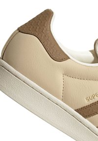 Beige and brown leather sneaker with textured heel tab, white sole, and partial "SUPER" branding on side.