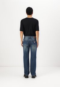 Zwarte T-shirt met korte mouwen, blauwe rechte spijkerbroek met een vervaagd uiterlijk, achterzakken en een leren merklabel, gedragen met zwarte schoenen.
