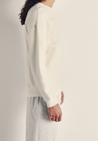 Vit texturerad sweatshirt med ribbad mudd och nederkant, med en rundad halsdesign. Kombinerad med ljusgrå sweatpants.