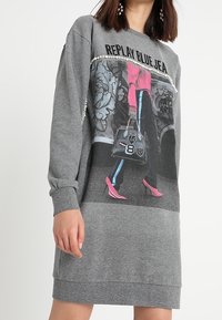 Vestido de sudadera gris con una imagen impresa de una persona en zapatos de tacón rosa y un bolso elegante, acentuado con detalles de perlas en el escote.