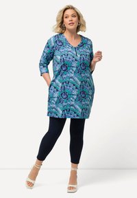 Tunique blu con motivo floreale, caratterizzata da scollatura a V e maniche a tre quarti. Indossata con leggings blu navy e décolleté bianchi con cinturino alla caviglia.