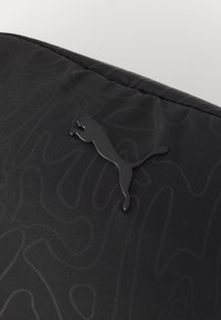 Svart tyg med ett subtilt vågmönster. Har en upphöjd svart Puma-logotyp som framhäver designens minimalistiska estetik.