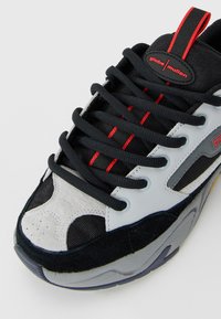 Black, gray, and white sneaker with black laces, red accents, and "globe mullen" label on the tongue, shown from a top-angle close-up.