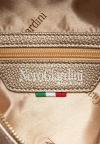 Guld tekstureret stofinteriør med en lynlås lomme, præget "NeroGiardini MADE IN ITALY," og en lille italiensk flag accent.