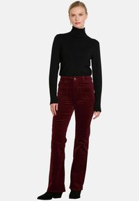 Pantalones acampanados de pana burdeos con una textura suave, cuatro bolsillos y cierre frontal de botón, combinados con un suéter negro ajustado de cuello alto.