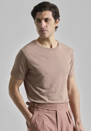 Camiseta de manga corta color marrón claro en una tela suave, con cuello redondo y un corte casual, combinada con pantalones rosas ajustados y un cinturón.