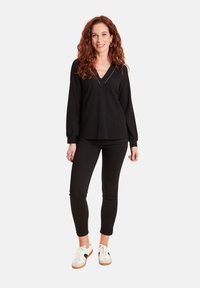 Haut noir à manches longues côtelé avec décolleté en V et couture blanche, associé à un pantalon noir slim et des baskets blanches avec des semelles brunes.