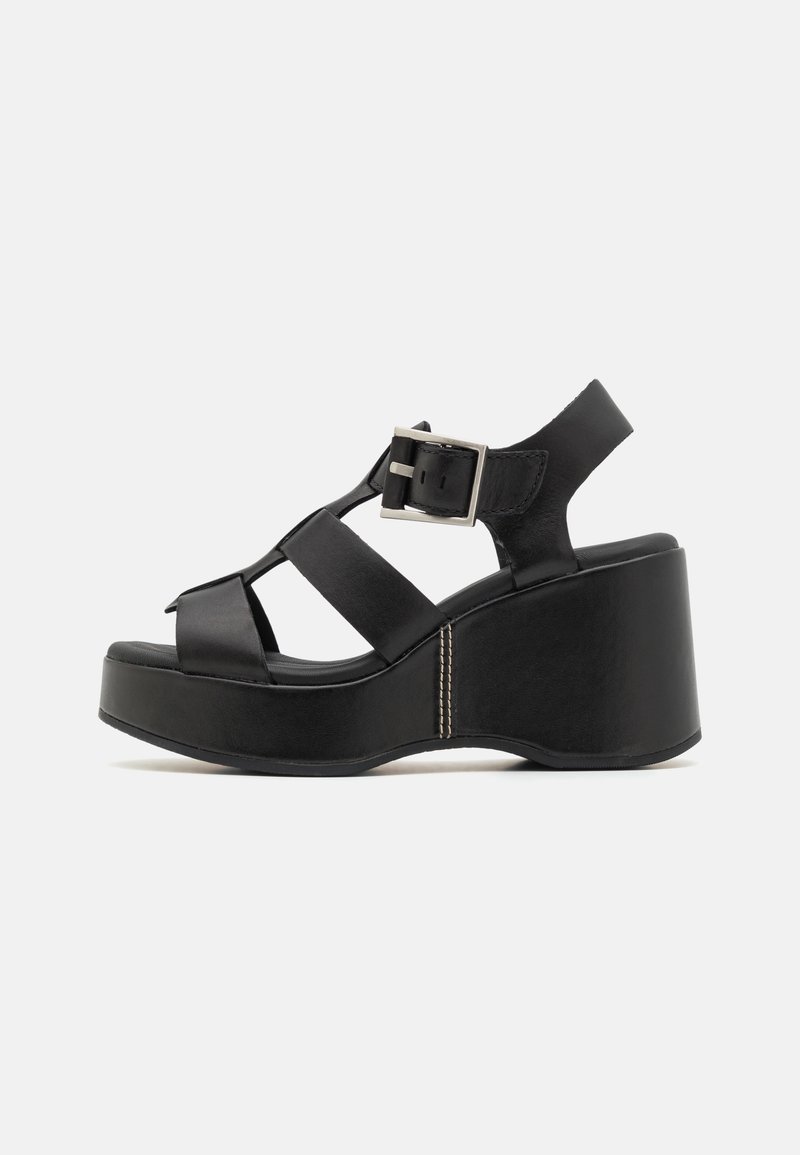 Sandale plateforme en cuir noir avec talon épais, larges brides, et une grande boucle argentée sur le côté.
