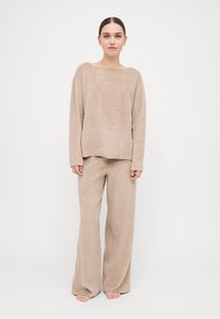 Beige loungewear set made of soft, textured fabric. The top has a wide neckline and long sleeves; the pants are wide-legged and relaxed fit.