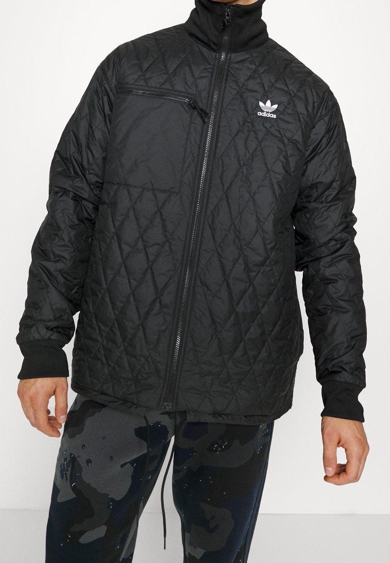 Svart kviltad jacka med ståkrage, utrustad med en dragkedjeförsedd bröstficka och stickade ärmslut. Logotyp på vänster bröst. Lättviktsmaterial.