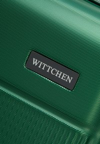 Green textured suitcase with a shiny finish, featuring a rectangular black label with the embossed brand name "Wittchen."