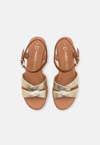 Sandalias de cuero marrón con una tira cruzada metálica dorada y detalle de nudo en la parte delantera. Correa de tobillo ajustable con una hebilla dorada. Talla 37.