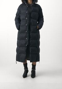 Dlouhá černá péřová bunda s knoflíkovým zapínáním, vysokým límcem, kapsami na zip a prošitým designem. Měkká, lehká tkanina.