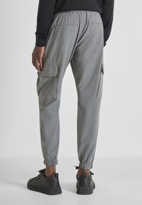 Grijze cargobroek met een relaxte pasvorm, elastische tailleband en boorden bij de enkels. Twee zijzakken en een gestructureerde stof creëren een casual uitstraling.