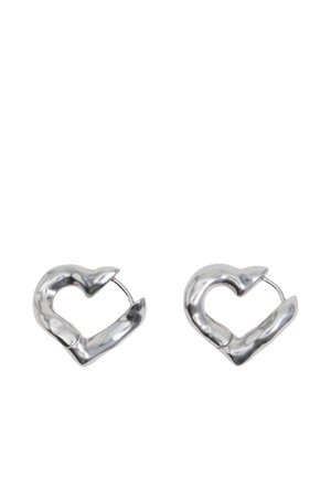 Pareja de pendientes de aro en forma de corazón plateados y brillantes con superficies irregulares y ligeramente retorcidas sobre un fondo blanco.