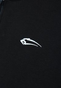 Un tessuto nero con una superficie liscia presenta un logo ricamato bianco che ricorda una forma stilizzata di onda o uccello.