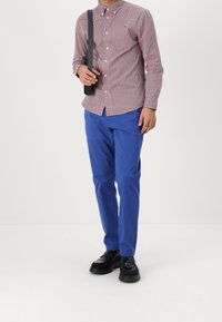 Long-sleeve checkered shirt in red and white, paired with blue trousers. Black shoes and a black shoulder bag complete the look.