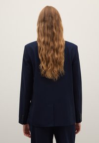 Blazer blu navy con design sartoriale, spacco singolo sul retro e polsini con bottoni, caratterizzato da tessuto liscio e forma strutturata.