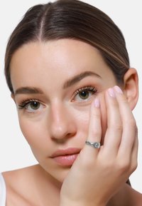 Zilveren ring met een gladde, gebogen vorm, getoond op een vinger nabij het gezicht van een model, waarbij de gepolijste textuur mooi contrasteert met de huidskleuren.