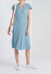 Abito midi azzurro chiaro con scollo a V e maniche corte, dotato di spacchi laterali e di un tessuto morbido e elasticizzato. Abbinato a sneaker bianche.