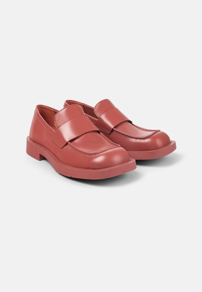 Red leather loafers with a wide strap across the instep, rounded toe, and thick rubber sole. Smooth texture with subtle stitching details.