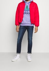 Röd puffjacka, ljuslila hoodiesweater med gröna ränder, mörkblå jeanstips, vita sneakers och vita strumpor med logotyp.