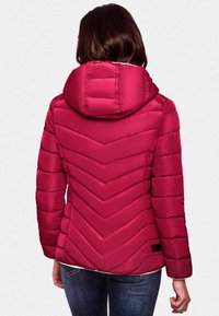 Fuchsia pufferjack met een chevronpatroon, voorzien van een capuchon en ribbelstructuur. Draag het over een lichte top, gecombineerd met blauwe jeans.