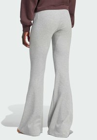 Sive flared trenerice napravljene od mekog materijala, s uskim strukom i širokim nogavicama koje sežu do tla. Glatka tekstura s minimalnim detaljima.