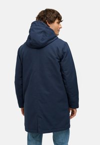 Námořnický modrý parka kabát s velkou kapucí, s rovný střih a viditelným prošitím. Hladká textilie a boční rozparky na lemu.