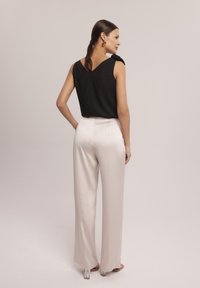 Czarna bezrękawnik z dekoltem w kształcie V z tyłu. Połączony z beżowymi, szerokimi spodniami z wysokim stanem. Gładki materiał z subtelnym połyskiem.