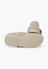 Chaussures en tissu beige avec un dessus texturé, deux brides Velcro et une semelle en caoutchouc motif floral.