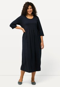 Ciemnoniebieska midi sukienka z rękawami 3/4, zbieranym wcięciem w talii i dwiema przednimi kieszeniami. Wykonana z miękkiego, elastycznego materiału. Gładka tekstura.