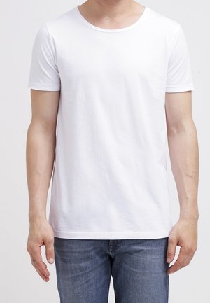 Camiseta blanca de manga corta hecha de algodón, con un escote redondo y una textura suave, combinada con jeans de mezclilla azul.