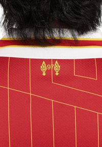 Maglia rossa con accenti gialli. Presenta un tessuto texturizzato, linee diagonali e un design che include due icone di fiamma con "97" sotto.