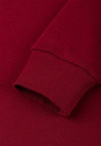 Burgundy neulemateriaali, jossa on ribbikäänteet, esittelee sileää pintaa ja tiukkaa muotoilua. Lähikuvassa korostuu ompeluyksityiskohtia.