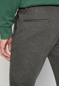 Gr�å joggerbukser med en struktureret overflade, med en baglomme og en behagelig elastisk talje, parret med en grøn sweatshirt.