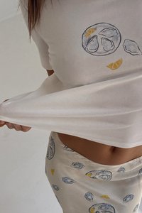 Hvit bomullstopp med østersmønster og gule detaljer; matchende skjørt med lignende design. Glatt tekstur, uformelt design, tettsittende stil.