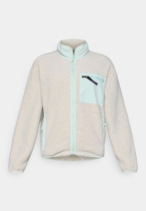 Helehall fleece-jakk kõrge kraega, millel on mündirohelise värvi lukk ja rinnatasku. Valmistatud pehmest materjalist, küljetaskutega.