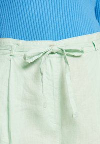 Ceinture en lin vert menthe avec un détail noué, associée à un haut bleu côtelé. Le tissu semble doux avec une texture légère et respirante.