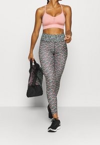 Sujeción deportiva rosa con detalles de malla, leggings estampados de flores en negro, rosa y azul, y una bolsa de gimnasio negra con flores; combinado con zapatillas negras.
